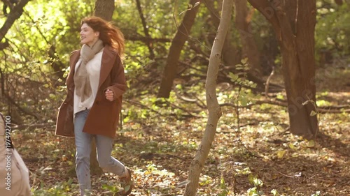 Red-haired woman in autumn park wearing coat, jeans and scarf