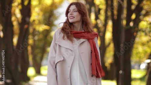 Red-haired woman in autumn park wearing coat, jeans and scarf