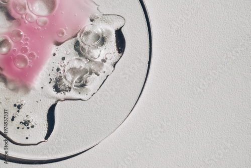 Pink and clear cosmetic serum, gel or liquid spreading with bubbles on petri dish