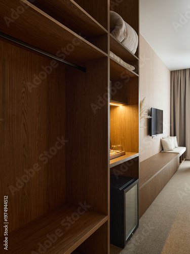 Modern hotel room interior with wooden wardrobe, long cabinet, and twin beds near a large window with sheer curtains. Warm beige tones and minimalist design.