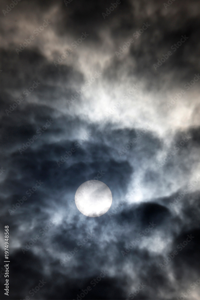 Fototapeta premium Sun pierces thick swirling clouds, golden glow amid dramatic daytime stormy sky layers. Bor et Bar. France.