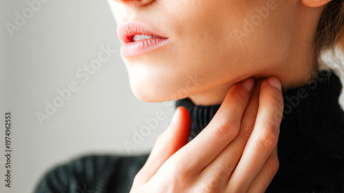 Woman in black sweater touching her throat with delicate fingers showing concern or discomfort in a soft natural light setting