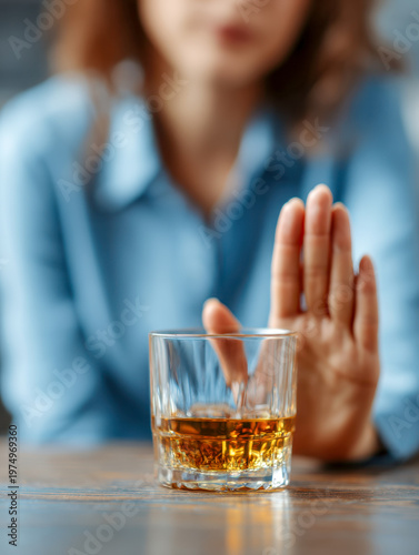 Woman refusing a glass of amber-colored liquor with an outstretched hand in a gesture of saying no and promoting sobriety and healthy choices