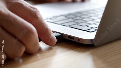 A person inserts a black cable connector into the side port of a modern portable computer