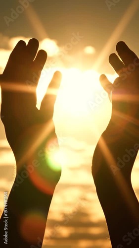 A silhouette of human hands reaching towards the bright golden sun during a beautiful sunset
