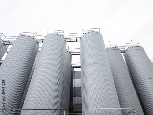 Low angle view of large industrial stainless steel silos and storage tanks at a food processing plant or brewery, modern manufacturing facility architecture