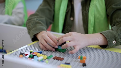 Hands of little boy in safe waistcoat playing with toy colorful blocks on the table in game center. Selective focus. Slow motion