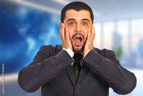 Man in suit looks shocked, hands on cheeks