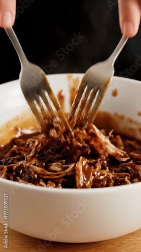 Two metal forks lift tender shredded meat covered in a rich savory brown sauce from a white bowl