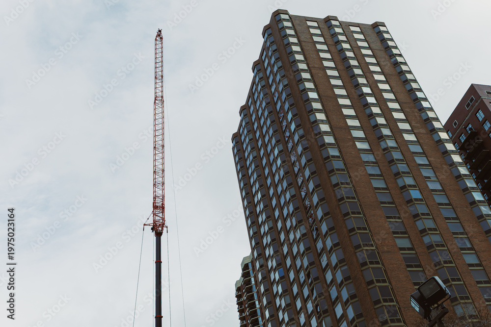 Fototapeta premium Construction site shows tall crane beside modern building in urban setting during cloudy day
