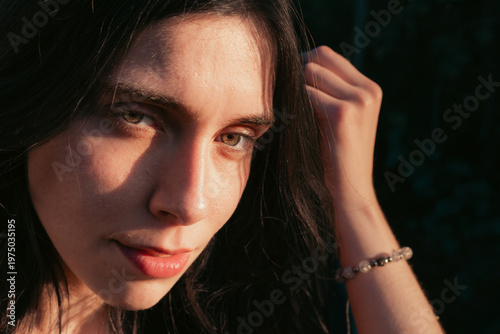 Close up portrait of young woman with hand in hair in warm sunlight