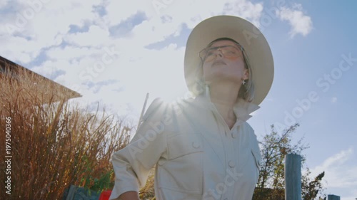 Confident Caucasian lady in cowboy hat. Low angle view portrait of a woman in orange sunglasses dazzled by sun.