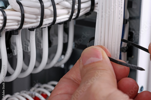 Installation of a plastic nylon tie on electrical insulated wiring wires in an electrical switchboard. 