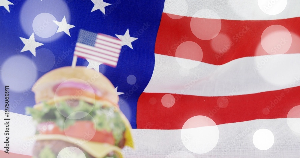 Fototapeta premium Displaying stacked cheeseburger with sesame bun and US flag toothpick on flag backdrop, copy space