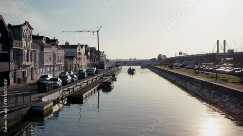 A traditional moliceiro boat glides along a calm canal in Aveiro, Portugal, flanked by elegant Art Nouveau facades and reflecting in the still water on a bright winter morning.