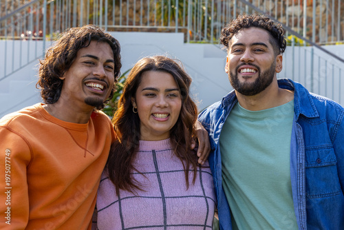 Three friends posing and smiling on exterior steps by metal railing with colorful clothing