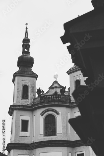 Black and white vertical shot of the Piarist Church of the Finding of the Holy Cross in Litomyšl, featuring baroque architecture and decorative statues, Czech Republic.