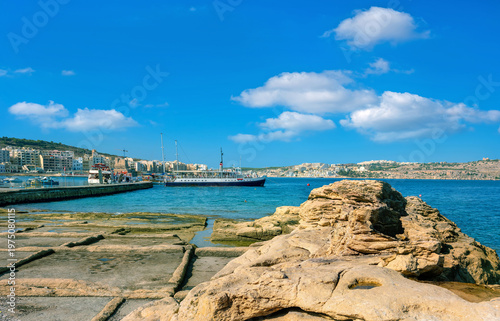 Seascape with rocky shore and wharf with moored touristic ships at St.Paul's bay. Bugibba, Malta