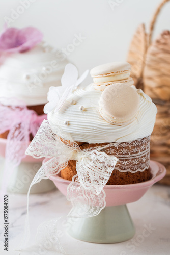 Easter cakes decorated with white cream, macaroons and edible violet flowers. Traditional sweet Easter bread on the stand with colorful painted eggs and straw bunny. Easter themed background