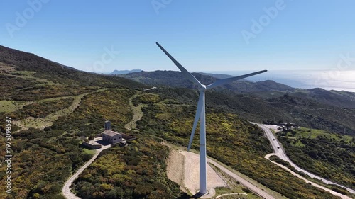 Aerial orbit around a wind turbine on a mountain ridge with a view of the Gibraltar strait in the Horizon.