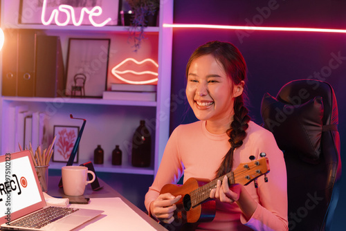 Canvastavla Host channel in musician of young beautiful Asian playing ukulele along singing, broadcasting on social media channel by phone at neon colorful light modern studio recording by camera