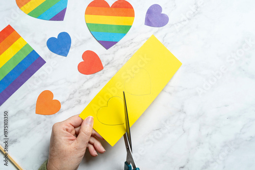Hand cutting yellow paper hearts on a marble background with rainbow and colorful hearts around