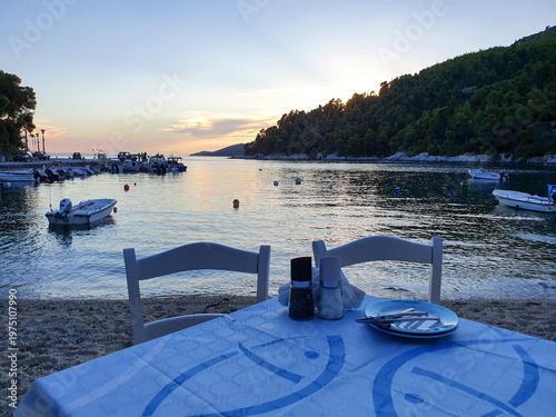 Bilde på lerret Seaside Dinner Table at Sunset Over Calm Harbor With Boats and Coastal Hillside