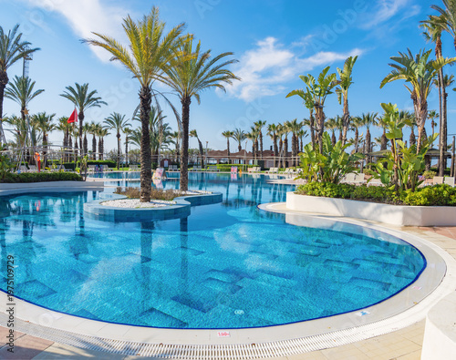 Obraz na płótnie Wide angle view of a stunning leisure area in a tropical hotel resort with elegant pool design, surrounded by sun loungers and palm trees under a bright summer sun, idyllic holiday in Turkey