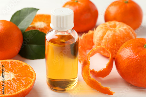 Bottle of tangerine essential oil and fruits on white wooden table, closeup