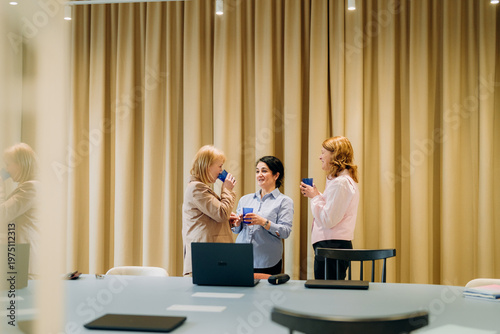 Tableau sur toile Three professional women share smiles and laughter in a well-lit conference room