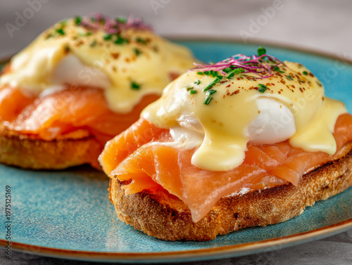 Two pieces of toasted bread topped with smoked salmon, poached eggs, creamy hollandaise sauce, and garnished with chopped chives and microgreens on a blue plate