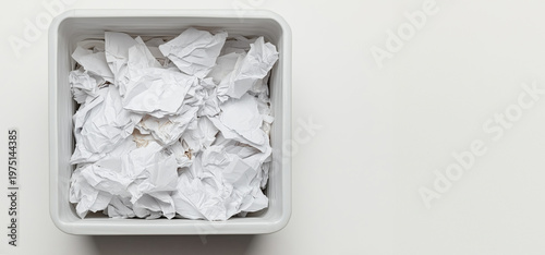 Crumpled paper pile in a square trash bin on a white background