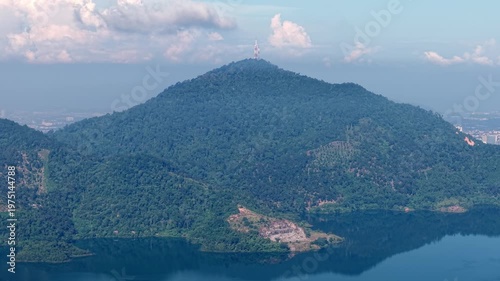 Mountain with a tall tower on top and a lake below at Mengkuang Dam. The mountain is surrounded by trees and the lake is calm
