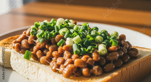 Close-up of natto served on white bread and topped with chopped green onions, showing a simple Japanese breakfast in warm light.