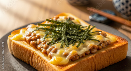 Close-up of toasted bread topped with natto, melted cheese, and shredded nori, capturing a warm savory Japanese-style snack.