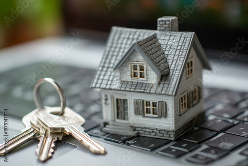 Small model house and metal keys placed on a laptop keyboard symbolizing online real estate search and digital home ownership concepts