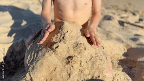 Creative child concentrating on building a sandcastle on a sunny beach during summer vacation. Enjoying a playful activity and engaging in outdoor fun by the sea while shaping wet sand with his hands