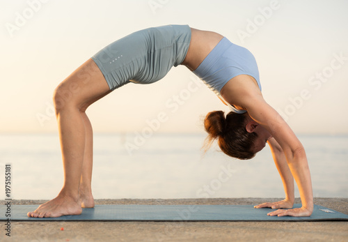 Photos Against background of sunset pinkening sky, slender silhouette of woman in sports clothes, hatha yoga lovers practicing oriental system of exercises