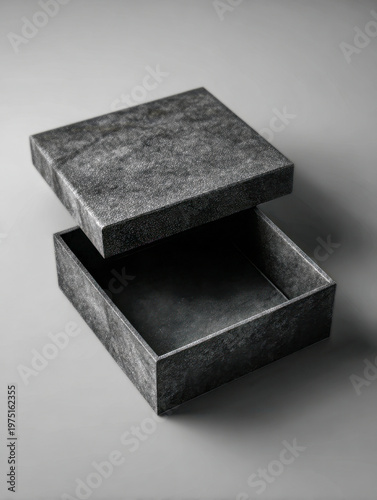 Textured dark grey empty square gift box with open lid photographed on plain gray surface with soft lighting and subtle shadows in studio setting