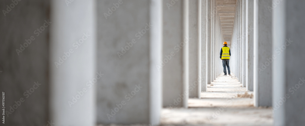 Fototapeta premium Construction worker walking through concrete pillars
