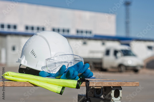 Fotografie Personal protective equipment PPE including a white helmet, transparent safety glasses, blue work gloves and a high-visibility yellow vest