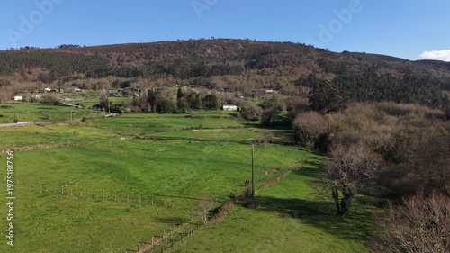 Green fields extending towards a small village nestled among hills and forests under a clear sky