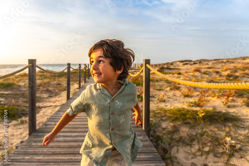 Joyful boy running on beach boardwalk at sunset