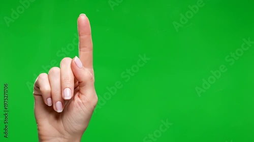 A close-up of a female hand with the index finger pointing up against a green screen, indicating direction or number one.