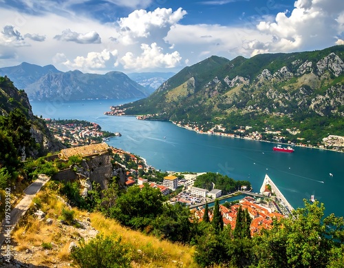 A scenic panoramic view of a coastal city nestled on a bay surrounded by lush, green mountains under a cloudy sky