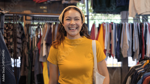 Young teen Gen Z asia female happy smile looking at camera at zero waste eco go green buy second hand sale store flea market mall thrift old used vintage fabric retro style. Woman people enjoy shop.