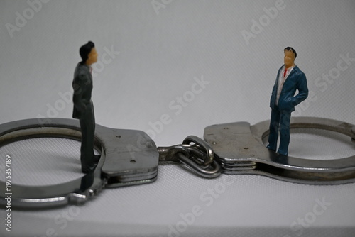 Two small professional figures positioned inside handcuff rings symbolizing corporate dispute or legal entrapment