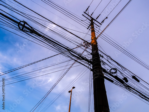 Wallpaper Mural Low-angle view of a utility pole with a dense network of overhead power and telecommunications lines in an urban area of Brazil, set against a cloudy blue sky.  Torontodigital.ca