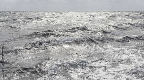 Vast ocean surface with shimmering water and frothy waves under a bright, overcast sky.