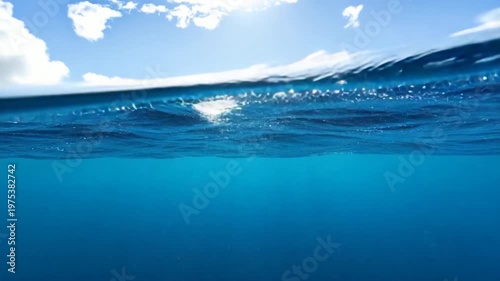 Split-level view of ocean water and sky with clouds and sun, showcasing a tranquil underwater scene